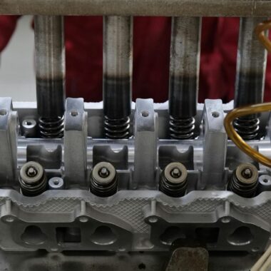Detailed view of a metallic engine cylinder head with springs and pistons, assembled in an industrial workshop.