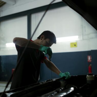 Mechanic checks engine oil in a car inside an auto garage, highlighting routine maintenance.